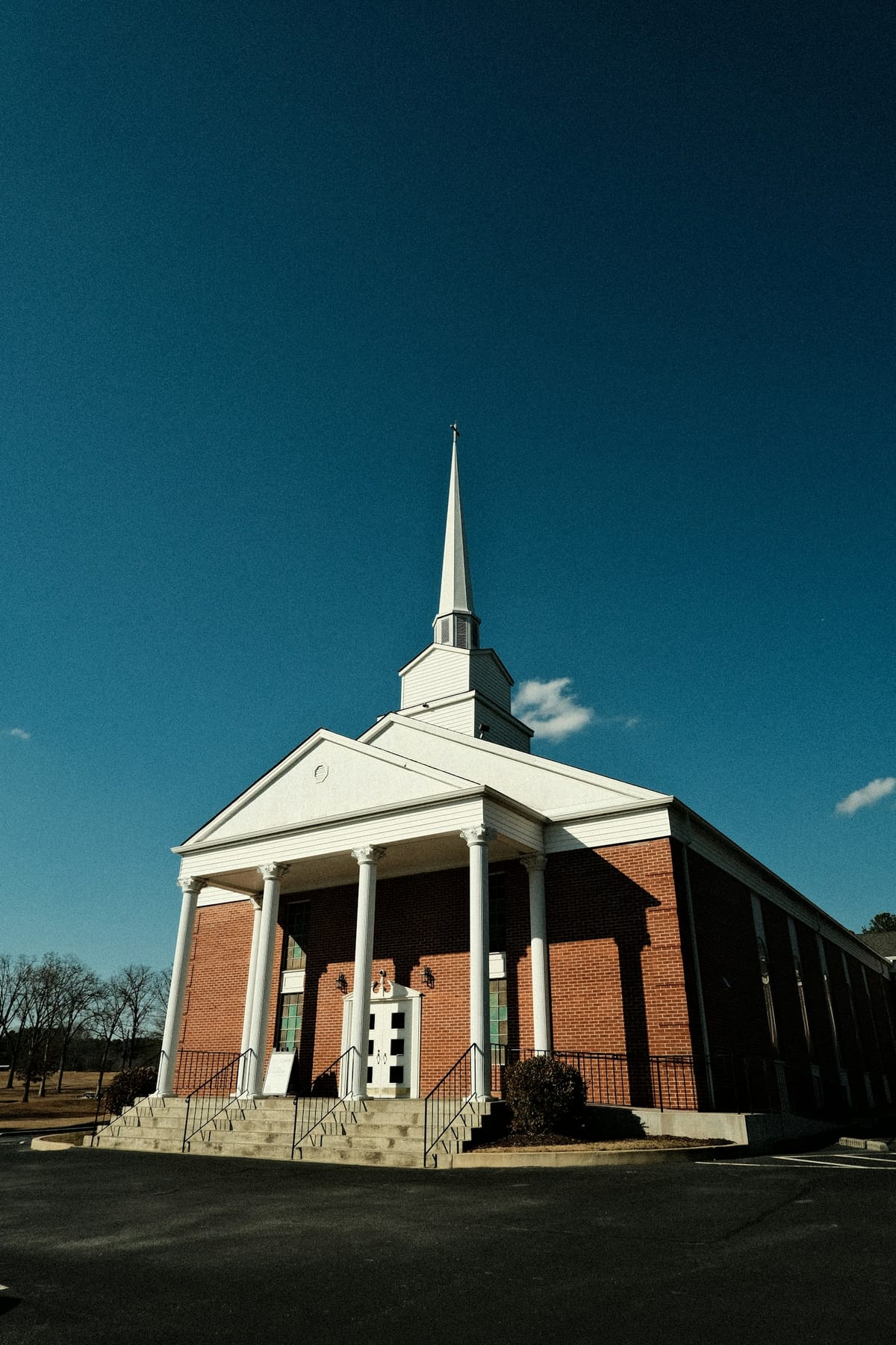 A brick church with white columns and a tall white steeple against a deep blue sky