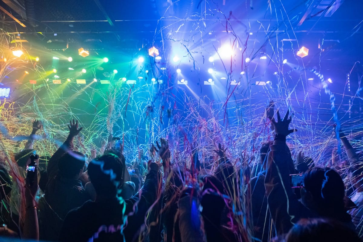 A crowd in silhouette under colorful lights and falling confetti
