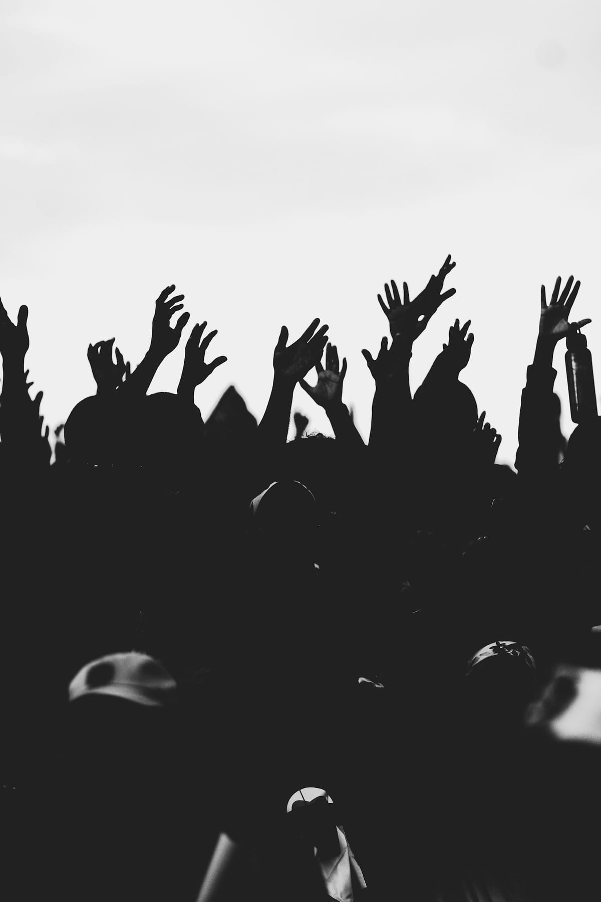Silhouetted hands raised against a pale sky, in black and white